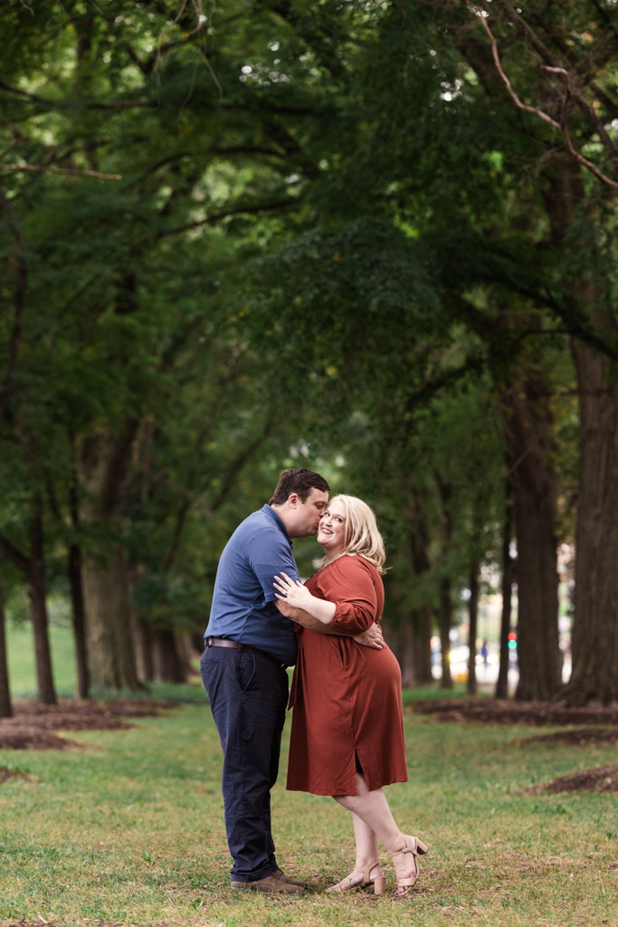 Engaged couple embracing and smiling in Grant Park surrounded by tall trees and greenery