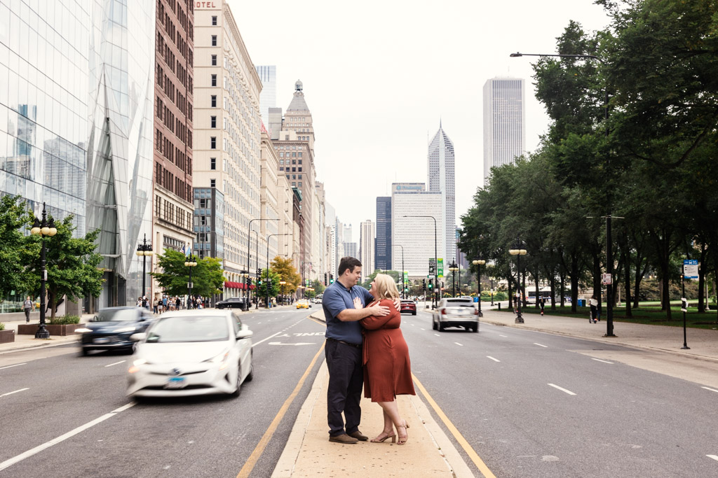 A couple holds each other on a city median in the South Loop, surrounded by downtown Chicago buildings and blurred cars rushing past them