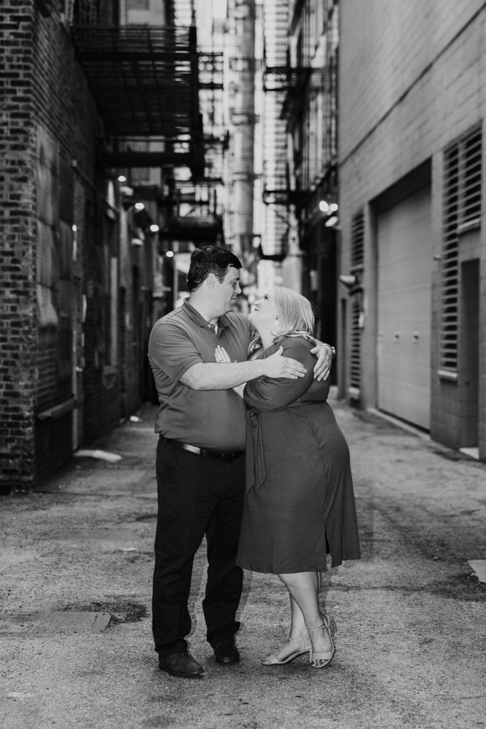 Black and white photo of engaged couple embracing and smiling at each other in a South Loop alleyway