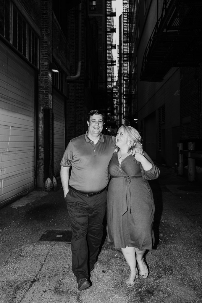 Black and white photo of happy couple walking arm-in-arm down an alley in downtown Chicago