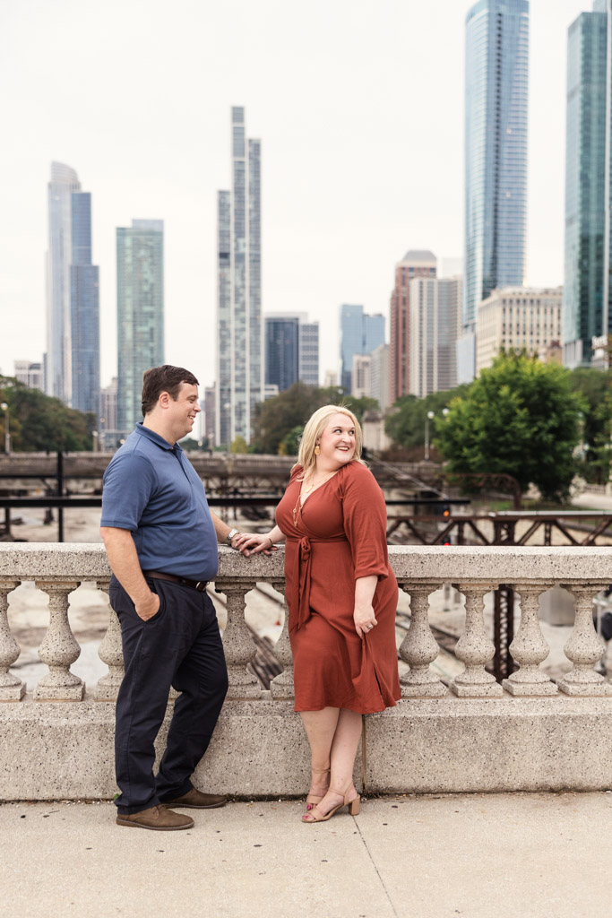 Engaged couple poses on a bridge in Grant Park with tall skyscrapers in the background