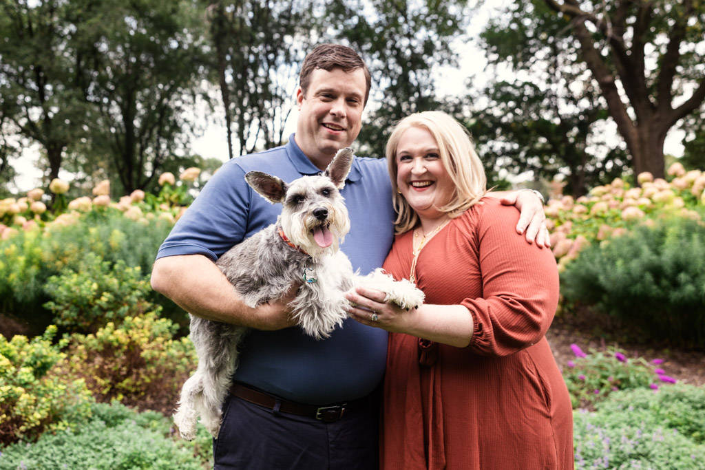 Portrait of happy couple and their dog outdoors during their South Loop engagement session with greenery in the background