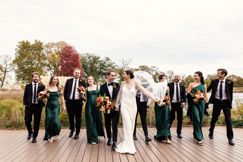 A bride and groom walk with their wedding party on a boardwalk in Lincoln Park before their Cafe Brauer wedding celebration