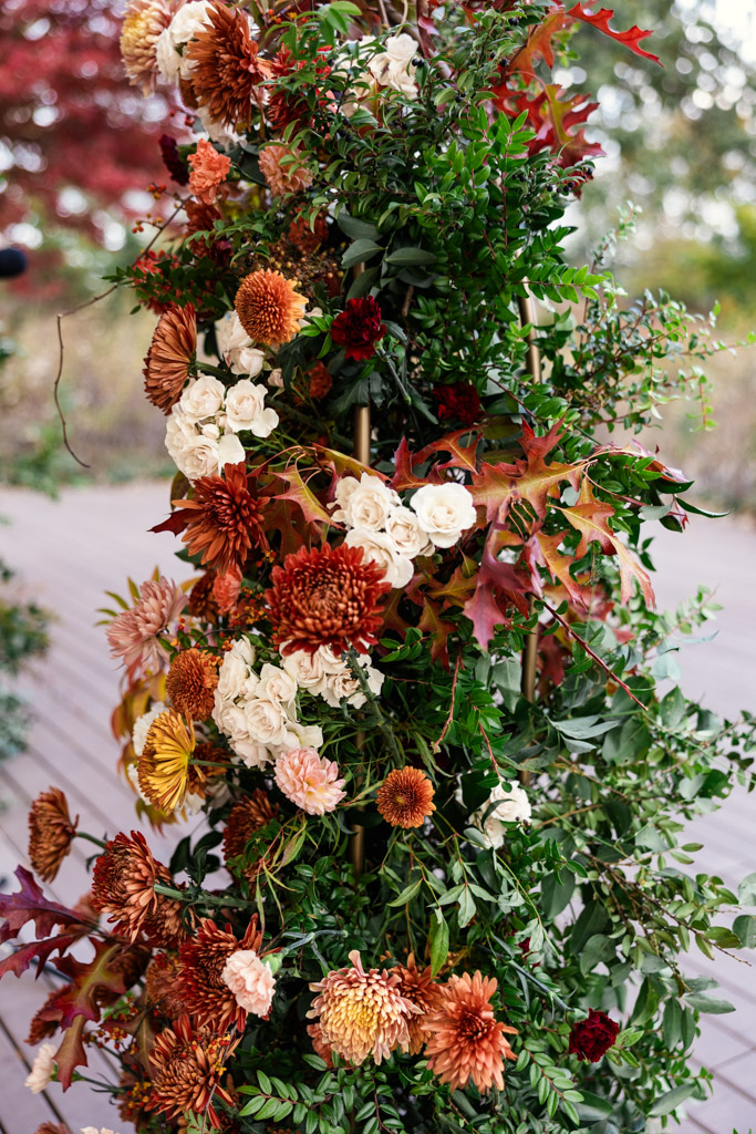 Autumn floral arrangement with orange, cream, and burgundy flowers, green leaves, and red-tinted foliage for a wedding ceremony at the Lincoln Park Honeycomb