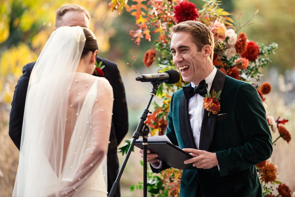 Groom in a tuxedo laughs while speaking to bride in a white dress and veil at their Lincoln Park Honeycomb wedding ceremony