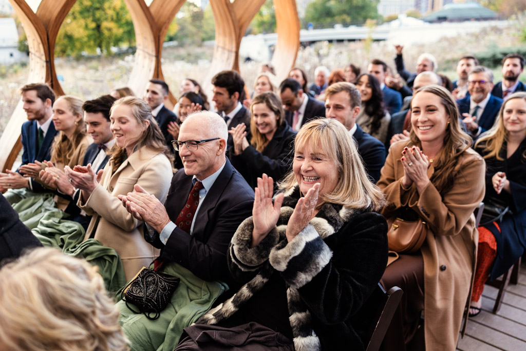 Guests sit and applaud at an autumn wedding ceremony under the Lincoln Park Honeycomb