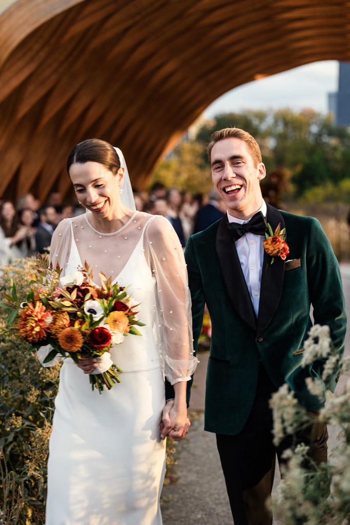 Bride and groom smiling and holding hands while walking outside after their wedding ceremony at the Lincoln Park Honeycomb