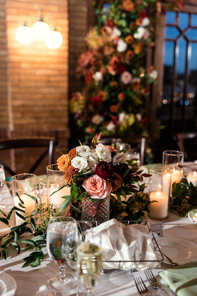 Guest table setting with floral centerpiece, candles, glasses, and folded napkins for wedding reception at Cafe Brauer
