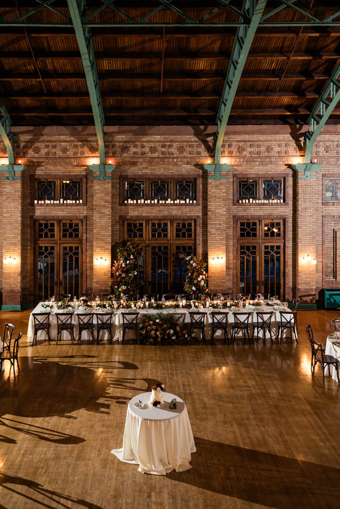 Wedding reception space at Cafe Brauer wedding, featuring a long dining table, floral arch, and a small round table in the foreground