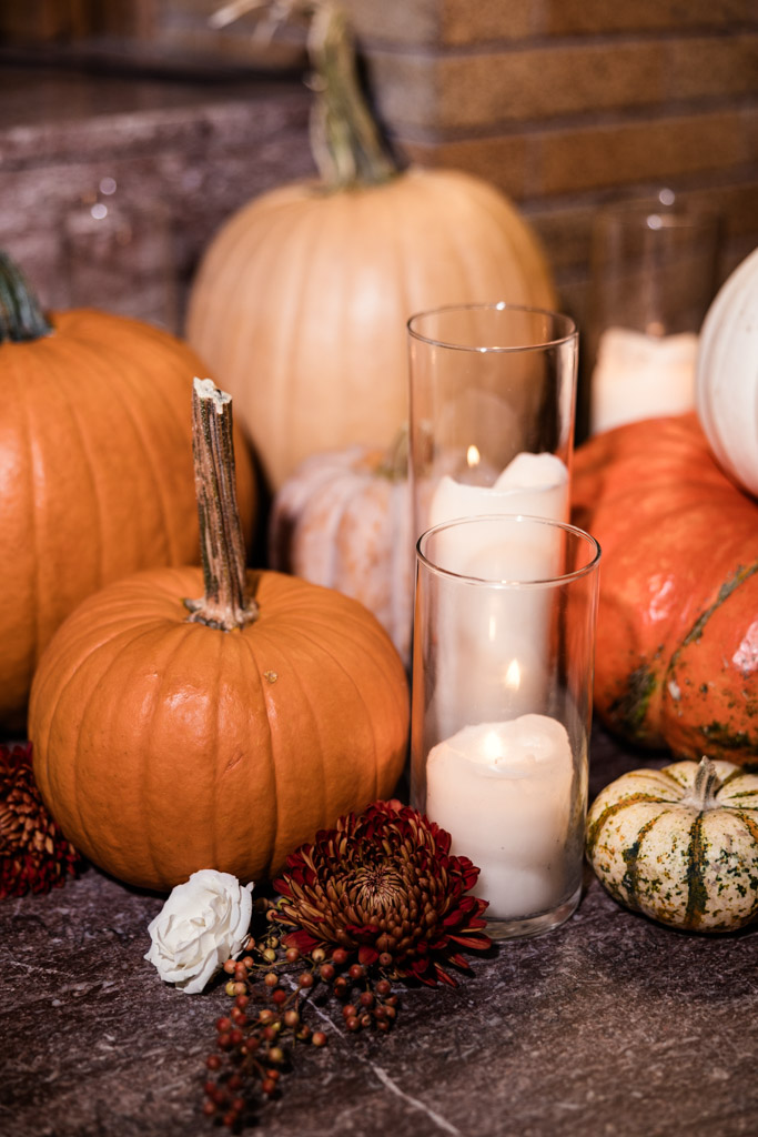 Various pumpkins, candles in glass holders, and autumn flowers arranged on a stone surface for fall wedding reception at Cafe Brauer
