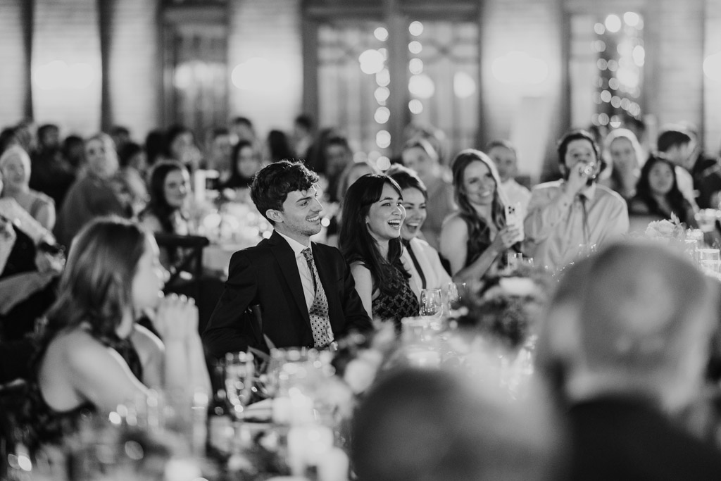Black and white photo of guests at tables smiling and laughing during Cafe Brauer wedding reception