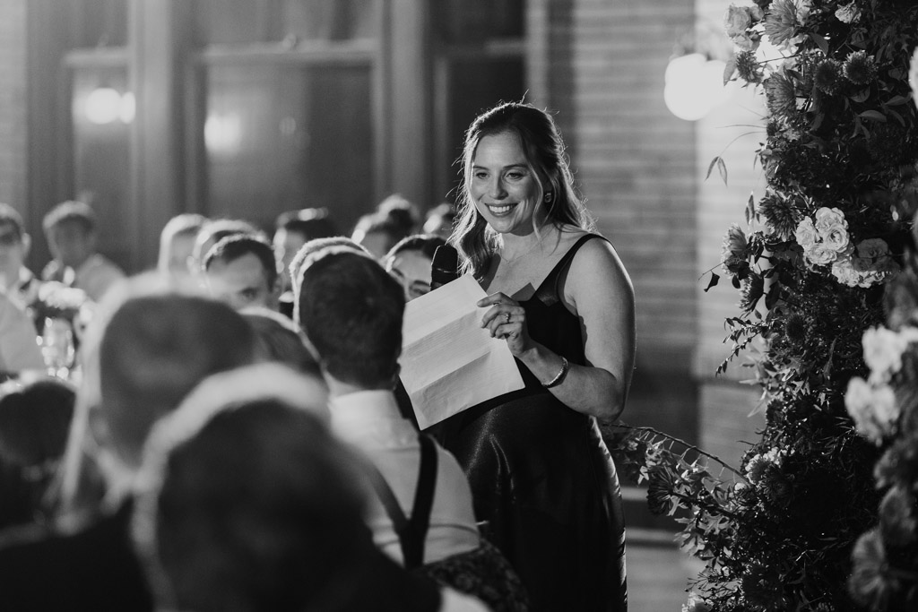 Black and white photo of Maid of Honor giving a speech at a Cafe Brauer wedding reception with guests listening.