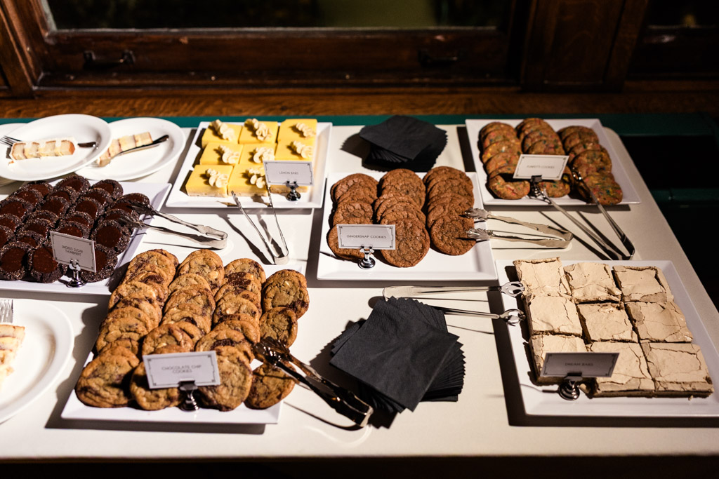 A dessert table at a Cafe Brauer wedding reception with assorted cookies, bars, and napkins artfully arranged on white plates