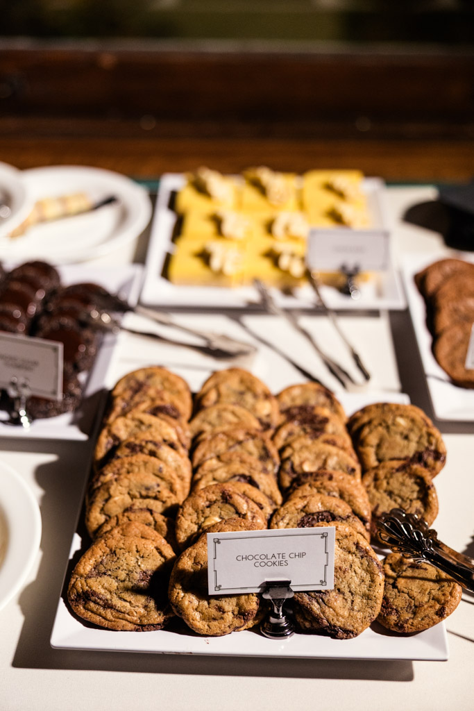 A platter of chocolate chip cookies sits on a table with other assorted cookies on the dessert table for Cafe Brauer wedding reception