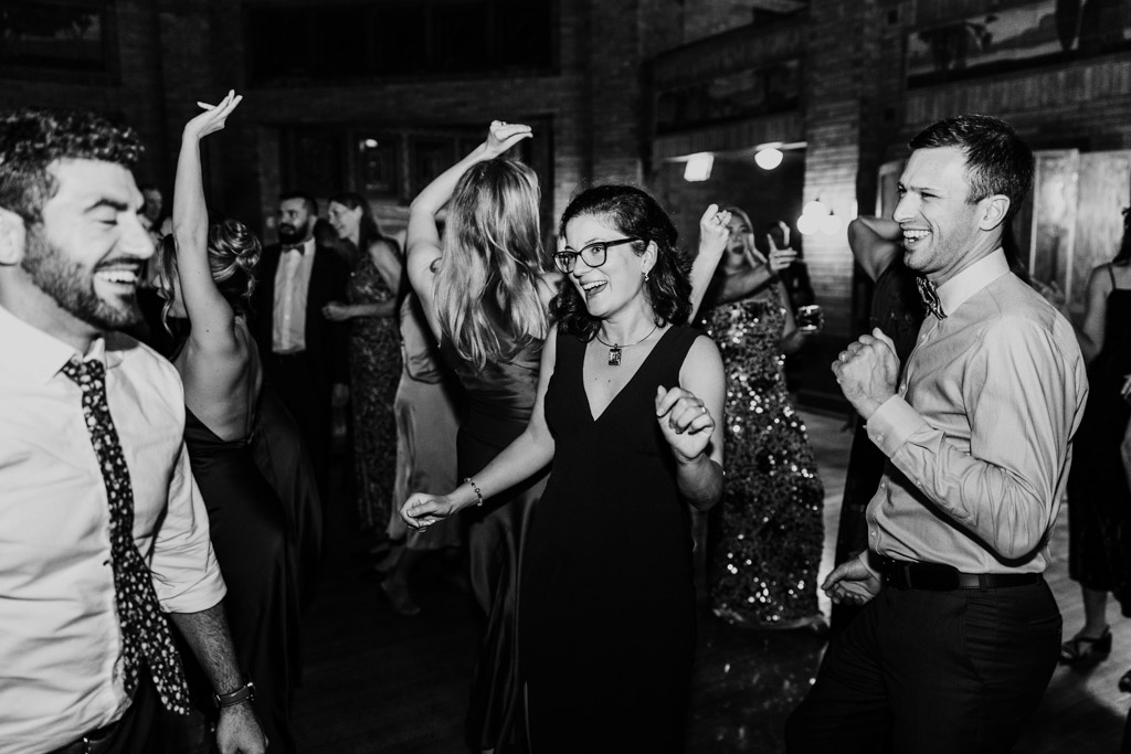 Black and white photo of guests smiling and dancing together at a Cafe Brauer wedding celebration, dressed in formal attire