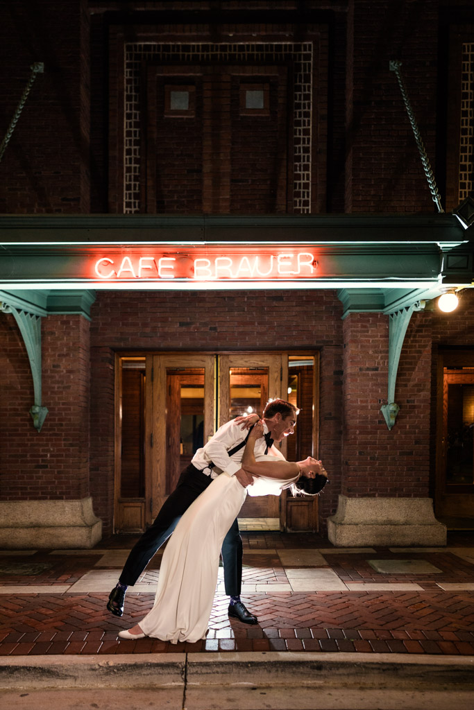 A groom dips his bride for a kiss at night beneath the glowing neon 