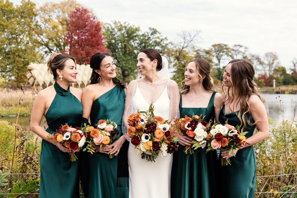 A bride in white stands in Lincoln Park with four bridesmaids in green dresses, all holding colorful flower bouquets