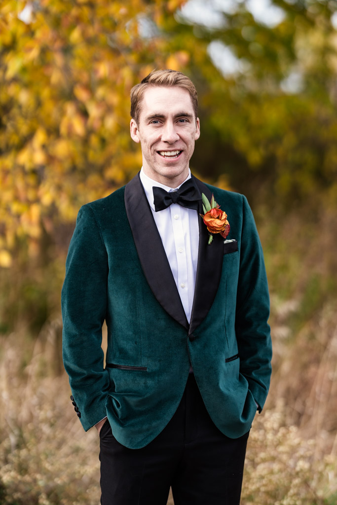 Portrait of groom in a green velvet tuxedo with a bow tie and boutonniere stands in Lincoln Park before his Cafe Brauer wedding