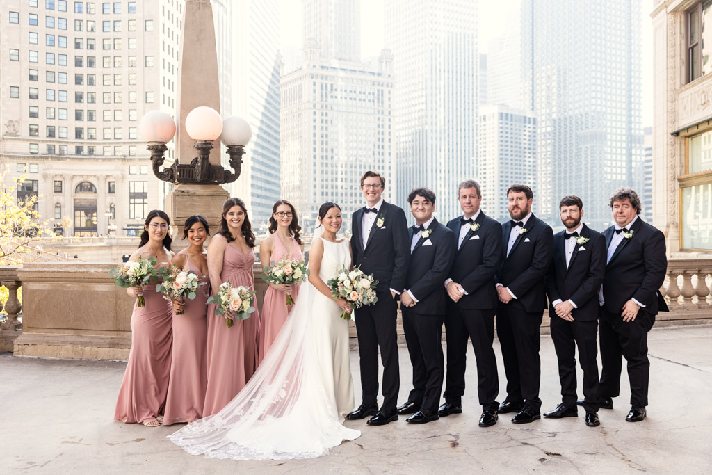 Portrait of wedding party poses near a bridge in formal attire with downtown Chicago buildings in the background