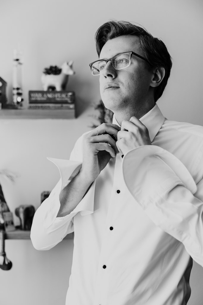 Black and white photo of groom buttoning his dress shirt, preparing forhis wedding celebration at Salvatore's