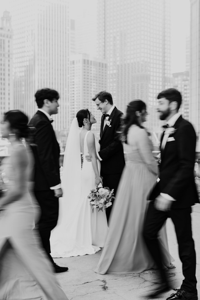 A bride and groom embrace outdoors near Salvatore's as blurred guests walk by, with tall city buildings in the background.