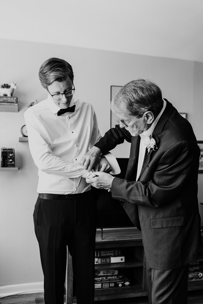 Black and white photo of groom's father helping groom with his cufflinks