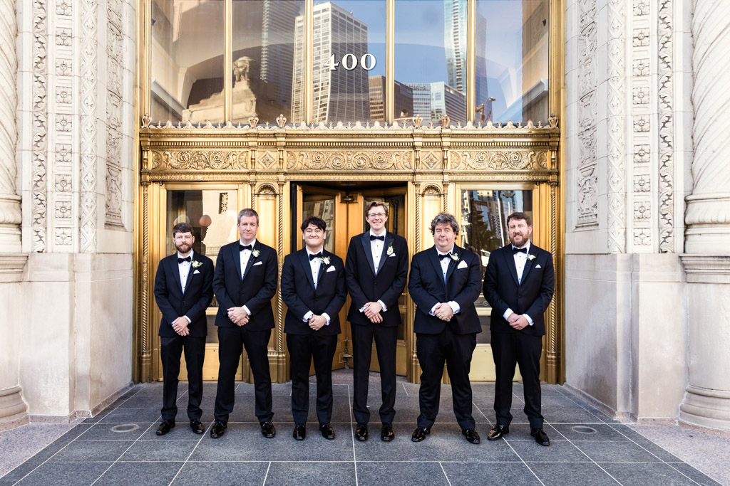 Portrait of groom and groosmen in tuxedos in front of the Wrigley Building's golden doors before wedding celebration at Salvatore's