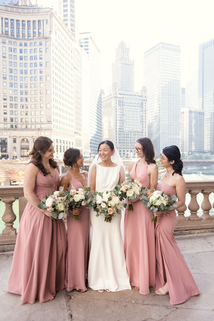 Bride in a white dress and four bridesmaids in pink gowns holding bouquets with downtown Chicago buildings in the background