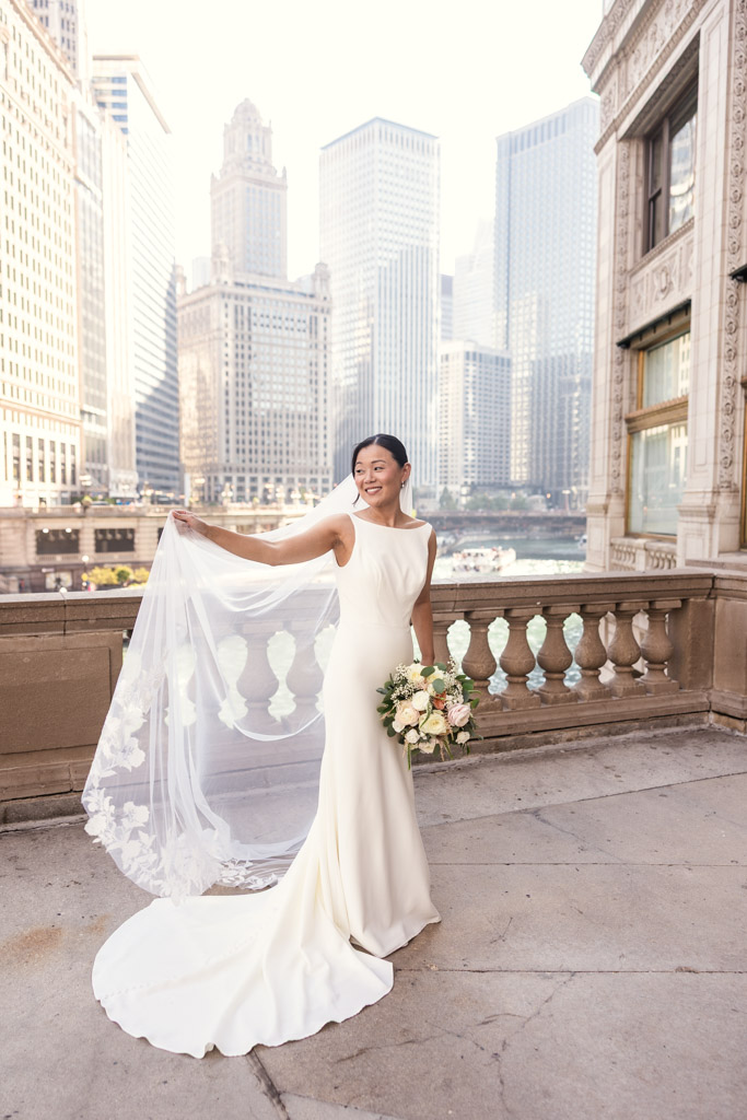 Portrait of bride in white dress and veil holds bouquet, standing outside the Wrigley Building in Chicago