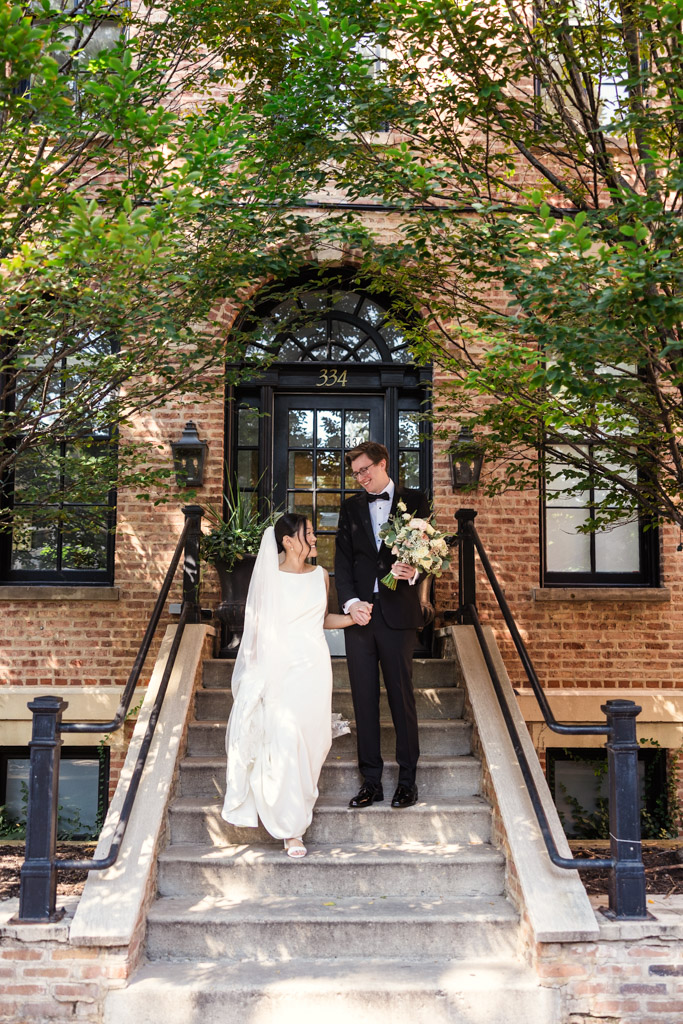 A bride and groom hold hands, walking down steps outside a brick building before their wedding celebration at Salvatore's in Chicago