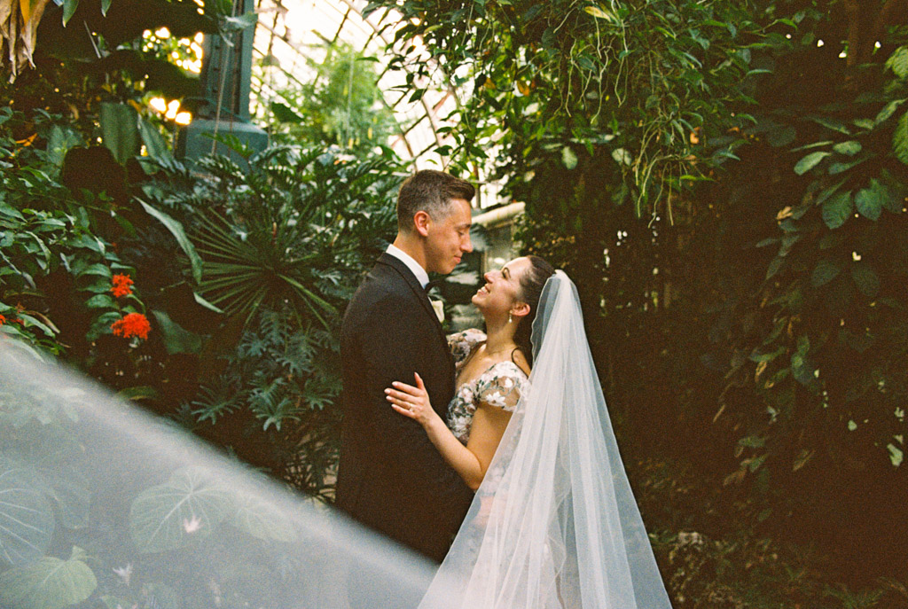 Film photo of bride and groom holding each other in the lush, green gardens of Lincoln Park Conservatory