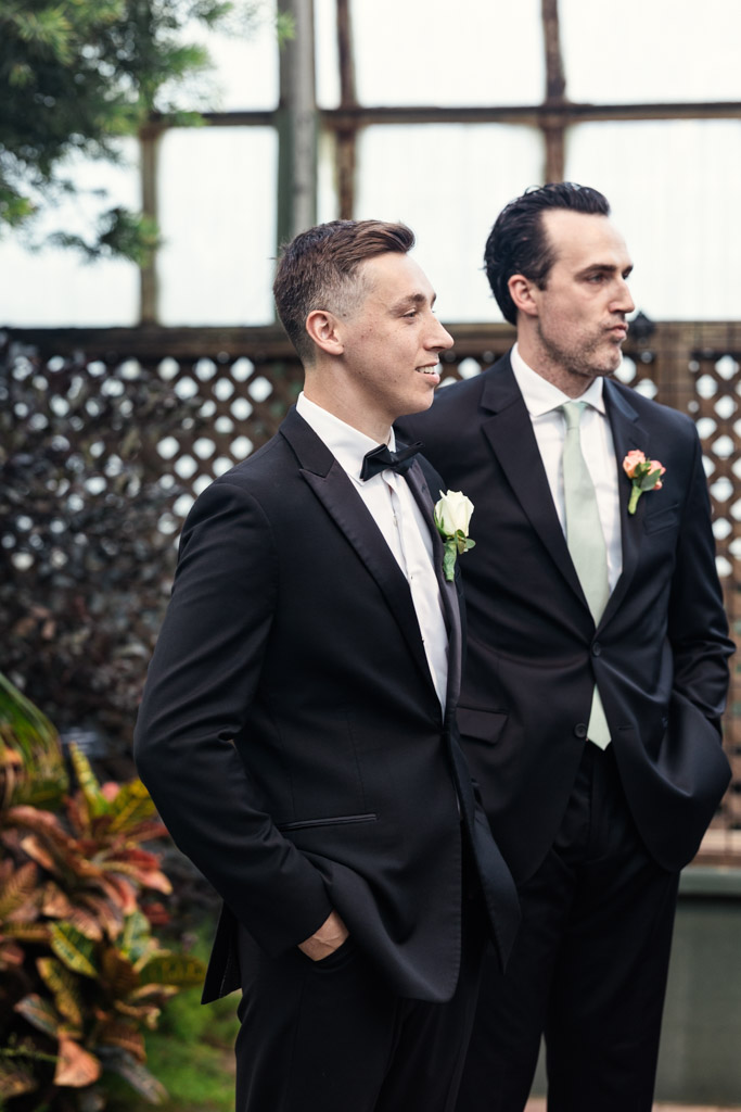 Groom and Best Man stand side by side, watching bride walk down the aisle at Lincoln Park Conservatory wedding ceremony