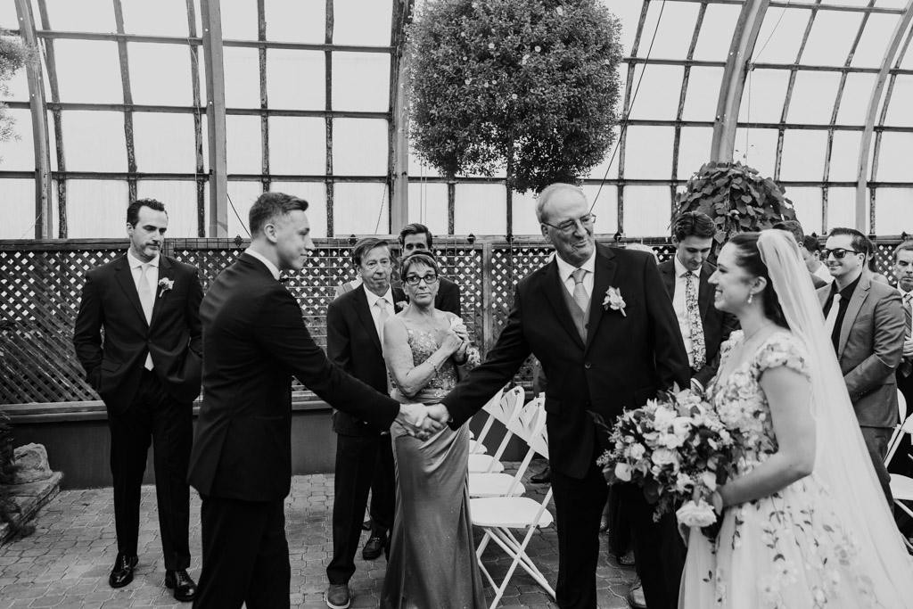 Black and white photo of bride’s father shaking hands with the groom during Lincoln Park Conservatory wedding ceremony