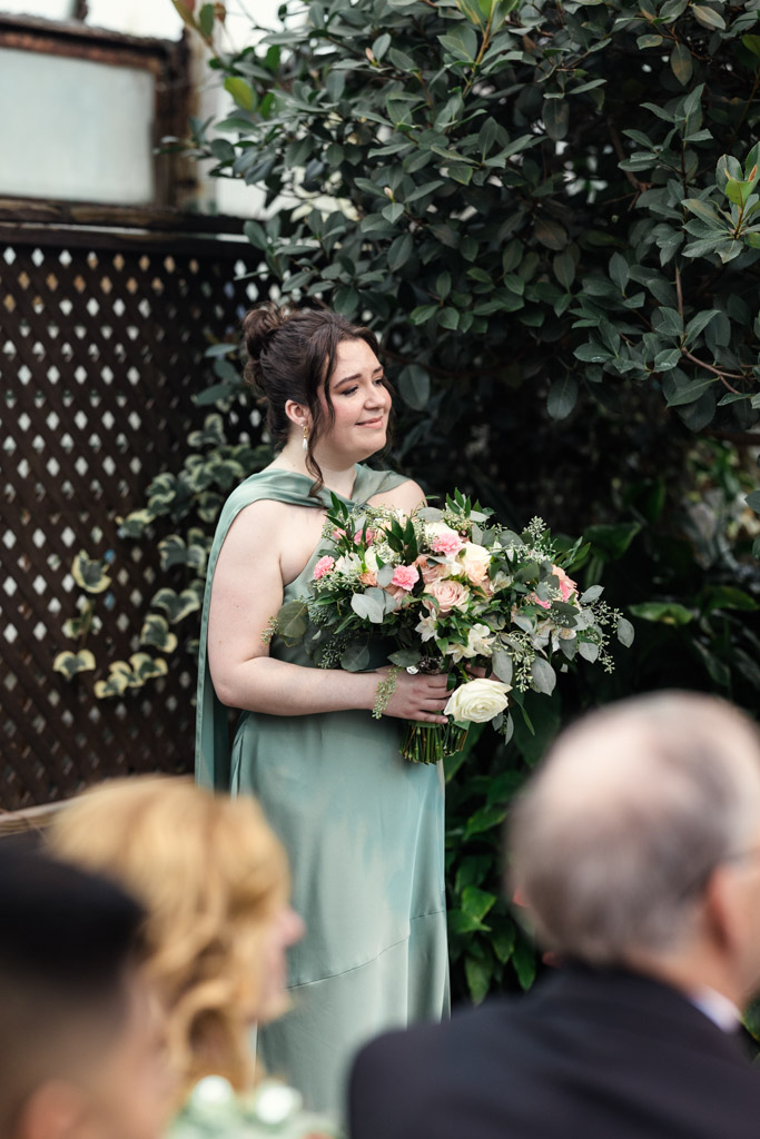 Maid of Honor in a light green dress holds a bouquet of flowers during Lincoln Park Conservatory wedding ceremony