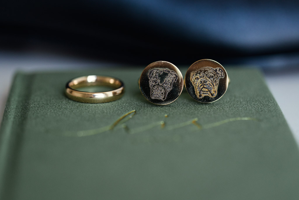 Groom's gold ring and cufflinks with dog engravings rest on a green vow book for Lincoln Park Conservatory wedding ceremony
