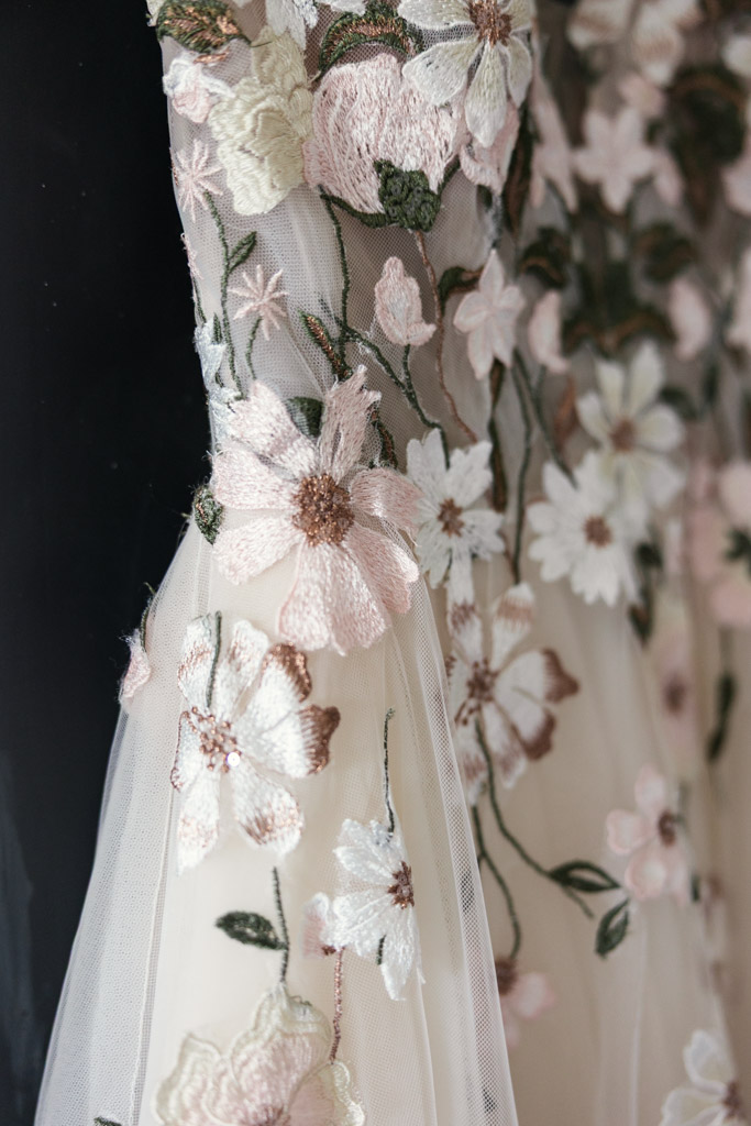 Detail photo of bride's dress — sheer fabric with embroidered pastel flowers and green leaves