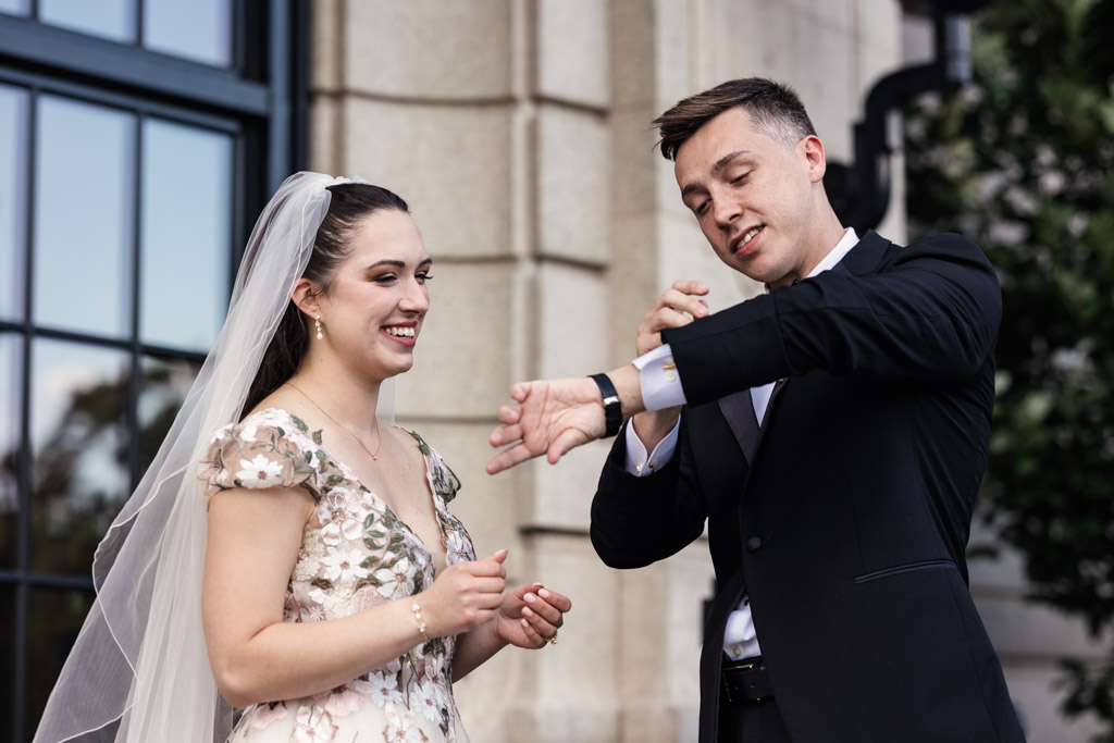Bride smiles as groom shows off his custom cufflinks during their first look before their Lincoln Park Conservatory, wedding ceremony