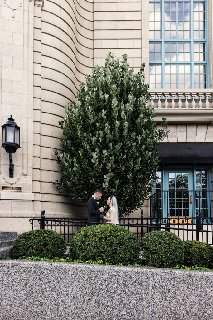 Groom reads his vows to bride as they stand together in front of a large tree outside The Belden-Stratford in Chicago