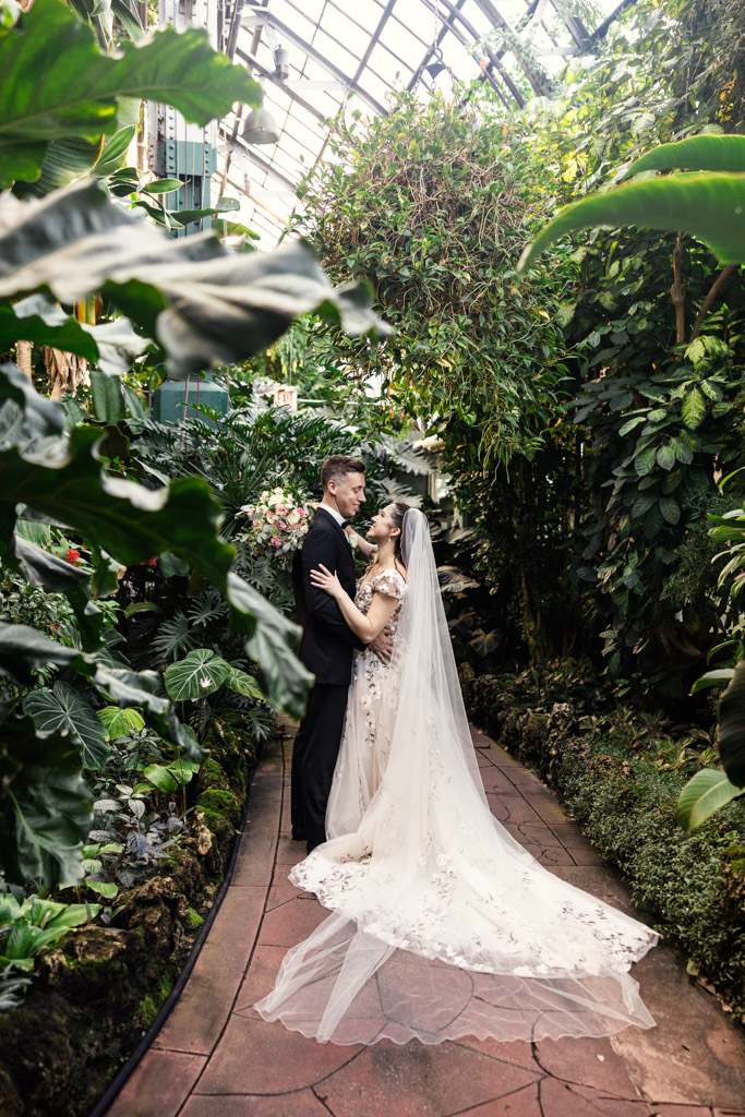 Bride and groom embrace in a lush greenhouse before their Lincoln Park Conservatory wedding ceremony, surrounded by vibrant green plants and natural light