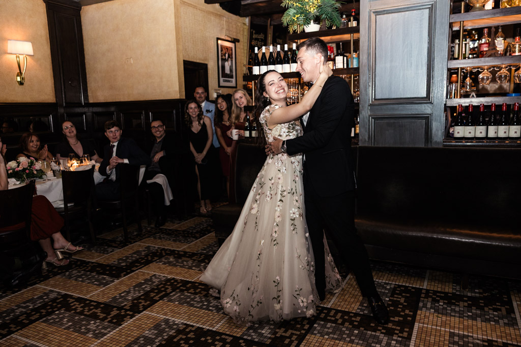 Bride and groom dance together as guests watch and smile in the warmly lit Mon Ami Gabi restaurant