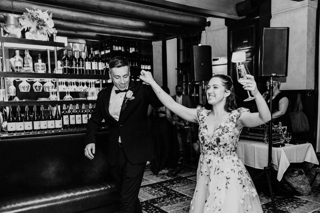 Happy newlywed couple in formal attire celebrate with raised hands and a toast in Mon Ami Gabi