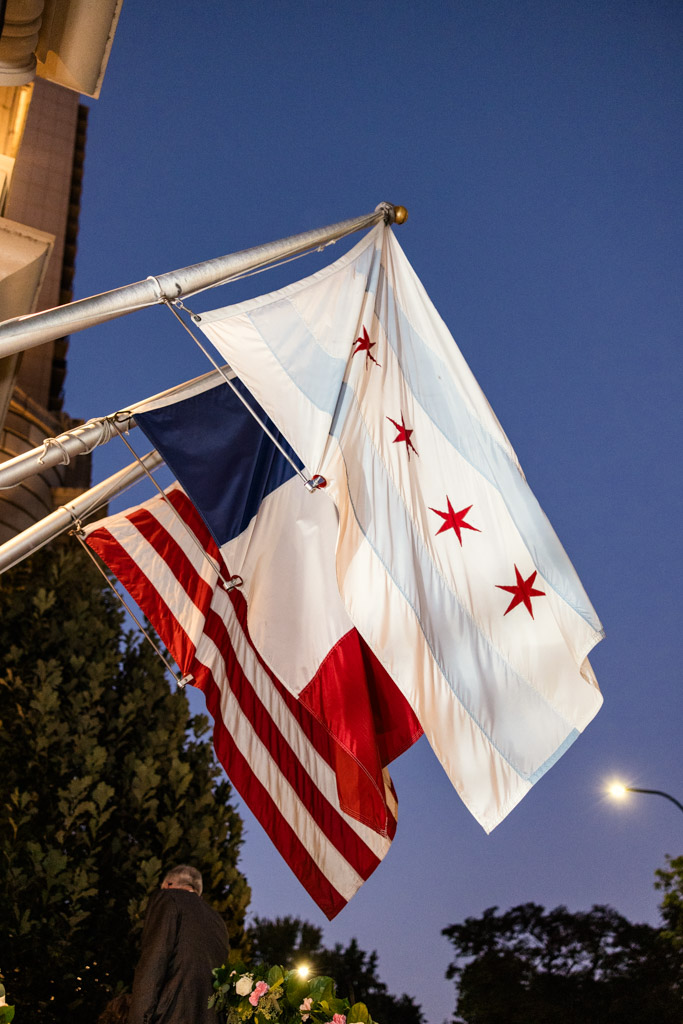 Three flags—Chicago, France, and the USA—hang on poles outside The Belden-Stratford at dusk