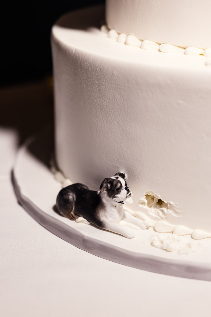 Small dog figurine appears to have chewed a hole in the side of a white frosted wedding cake for Mon Ami Gabi wedding reception