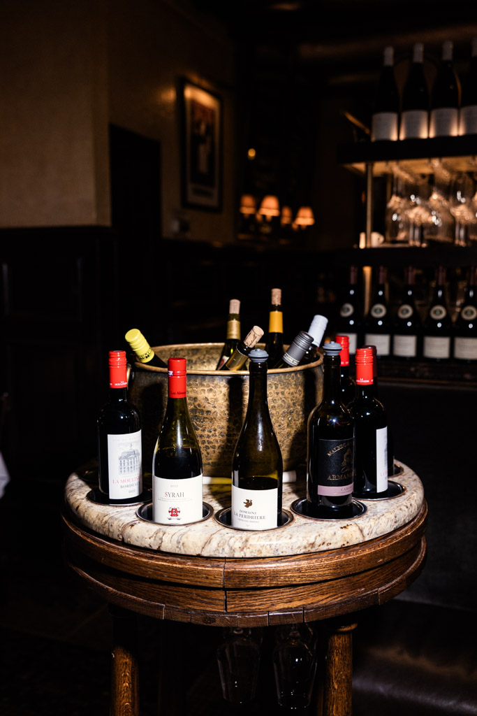 A round table with assorted wine bottles and an ice bucket at Mon Ami Gabi