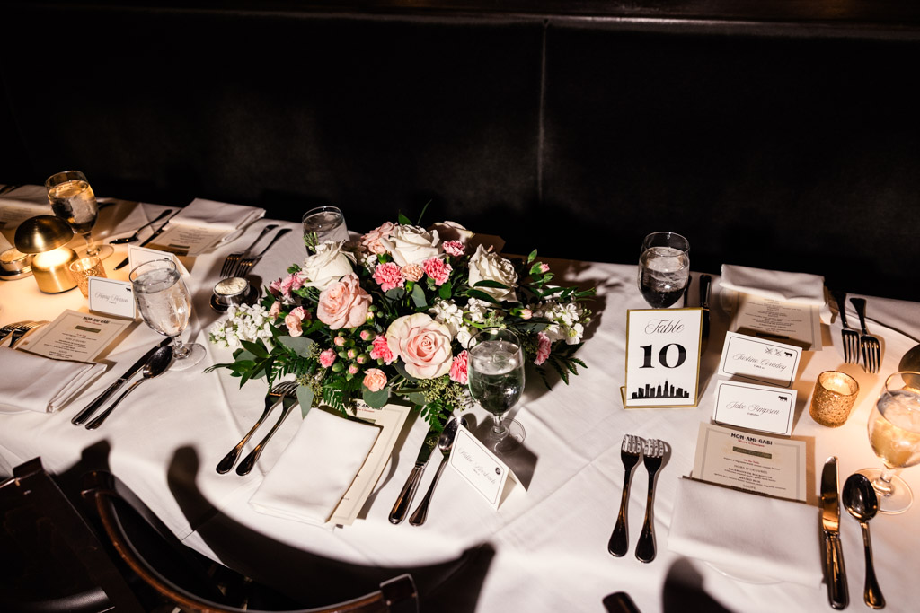 Guest table setting with floral centerpiece, menus, candles, and table sign on a white tablecloth for Mon Ami Gabi wedding reception