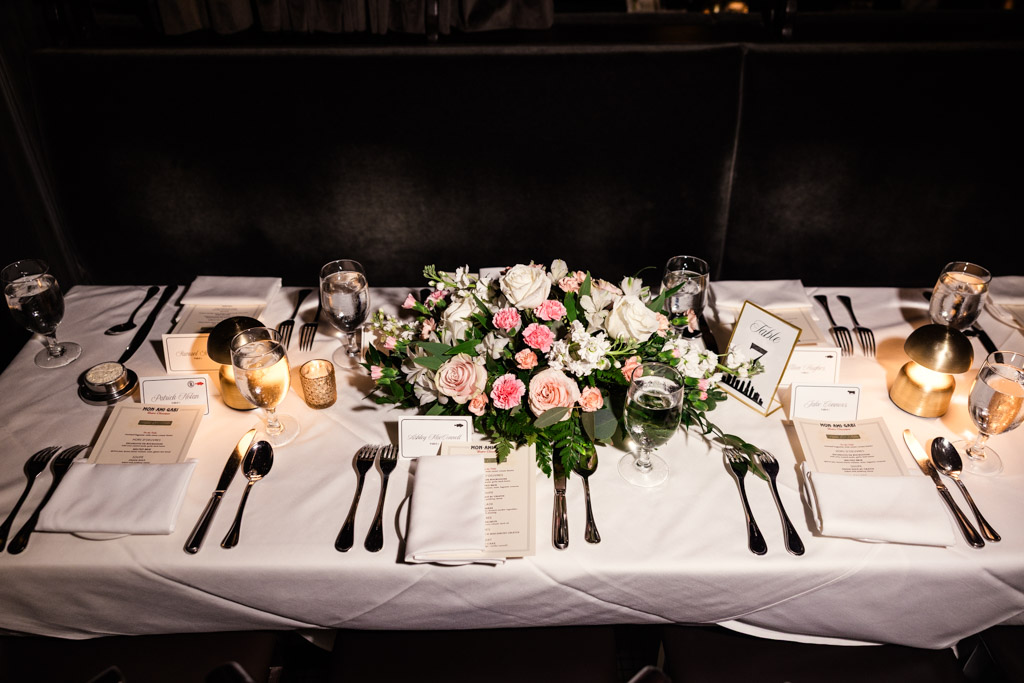 Guest dinner table set with floral centerpiece, menus, candles, and neatly arranged cutlery on white tablecloth at Mon Ami Gabi