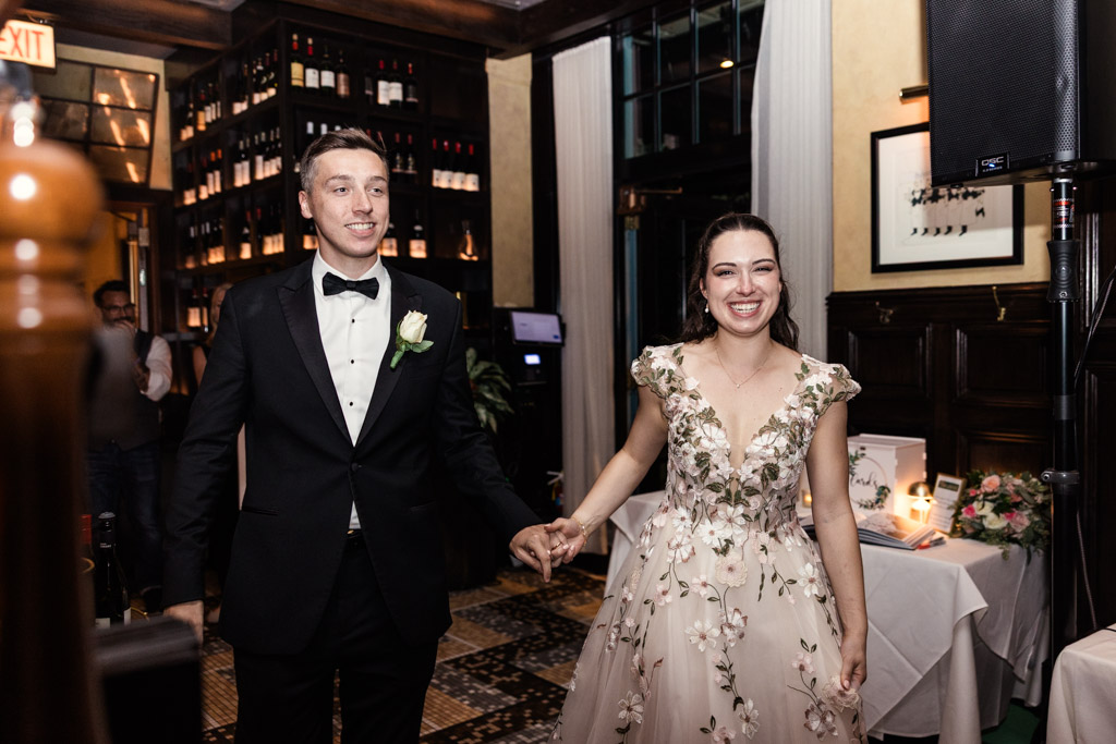 Newlyweds in formal attire hold hands and enter their wedding reception at Mon Ami Gabi