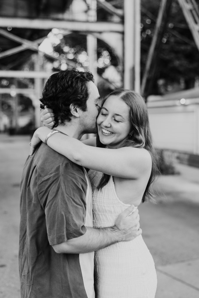 Black and white photo of man kissing his partner on the cheek as they embrace outdoors during their Roscoe Village engagement session