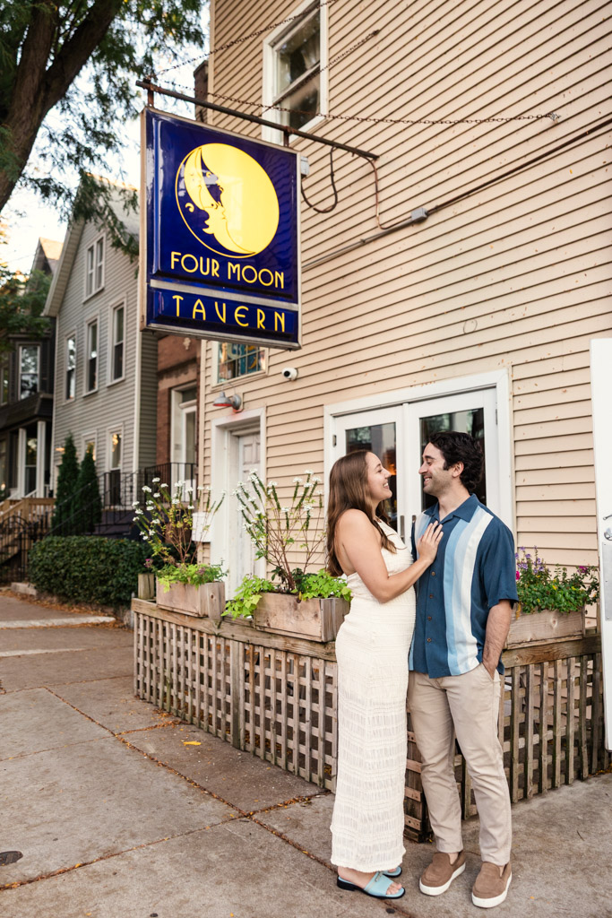 Happy couple smiles at each other outside Four Moon Tavern during Roscoe Village engagement session