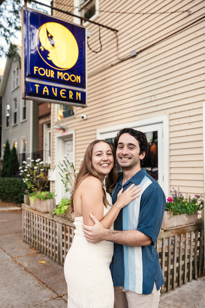 Happy engaged couple poses outside Four Moon Tavern in Roscoe Village